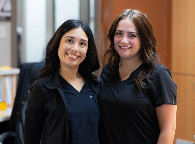 Two smiling female orthodontic staff members standing together in a professional office setting.
