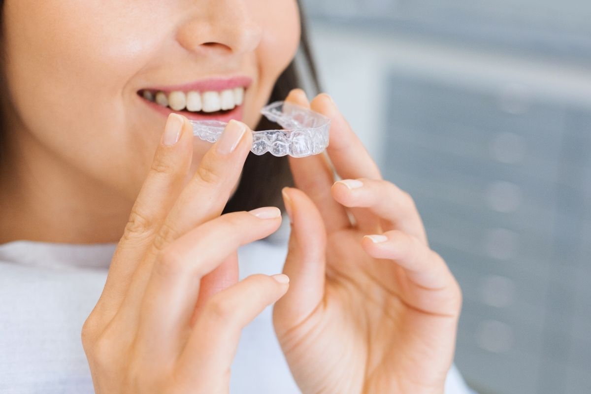 Close-up of a smiling woman holding an Invisalign tray, demonstrating the first step of treatment in a Dallas dental office.