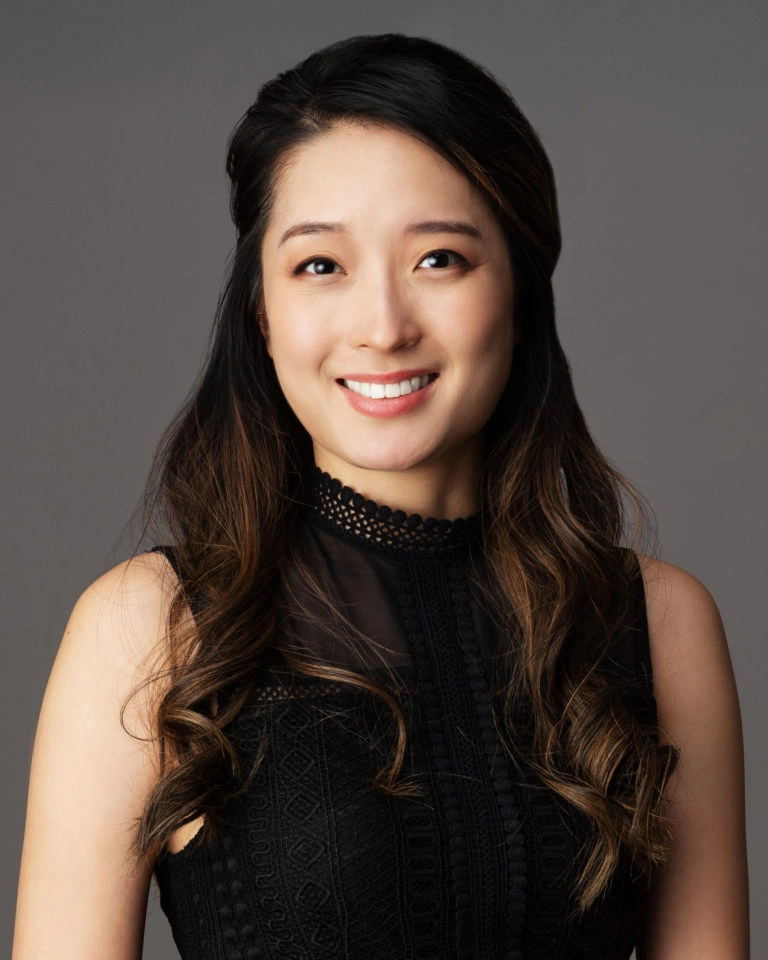 Professional headshot of smiling woman with long dark hair against gray background.