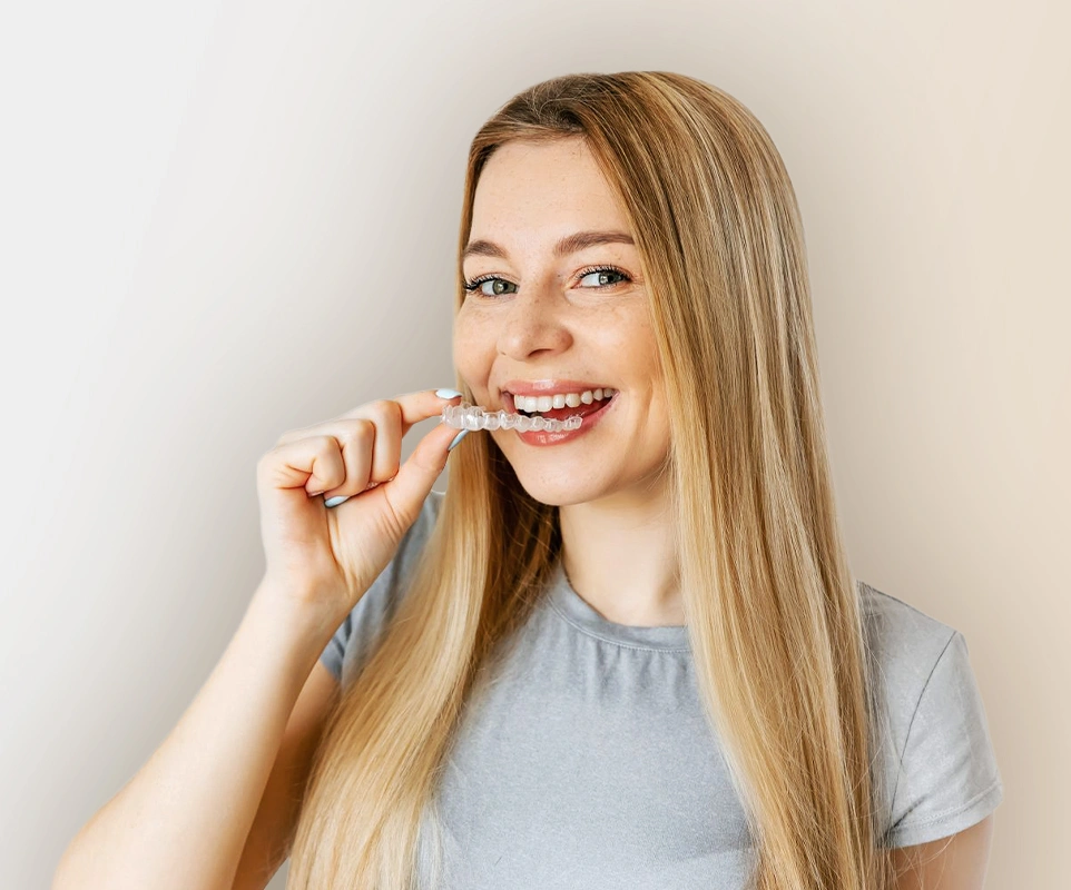 Young woman brushing teeth, smiling at camera against white background, dental care setting.