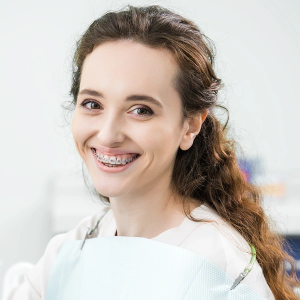 Smiling woman in white shirt against blurred background at orthodontics office.
