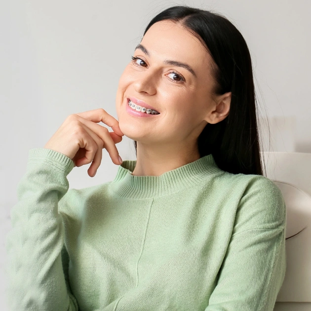 Woman in green sweater smiling thoughtfully against white background, orthodontics context.
