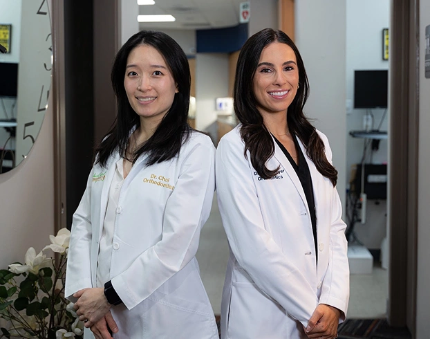 Two female orthodontists in white coats smiling in a modern dental office clinic.