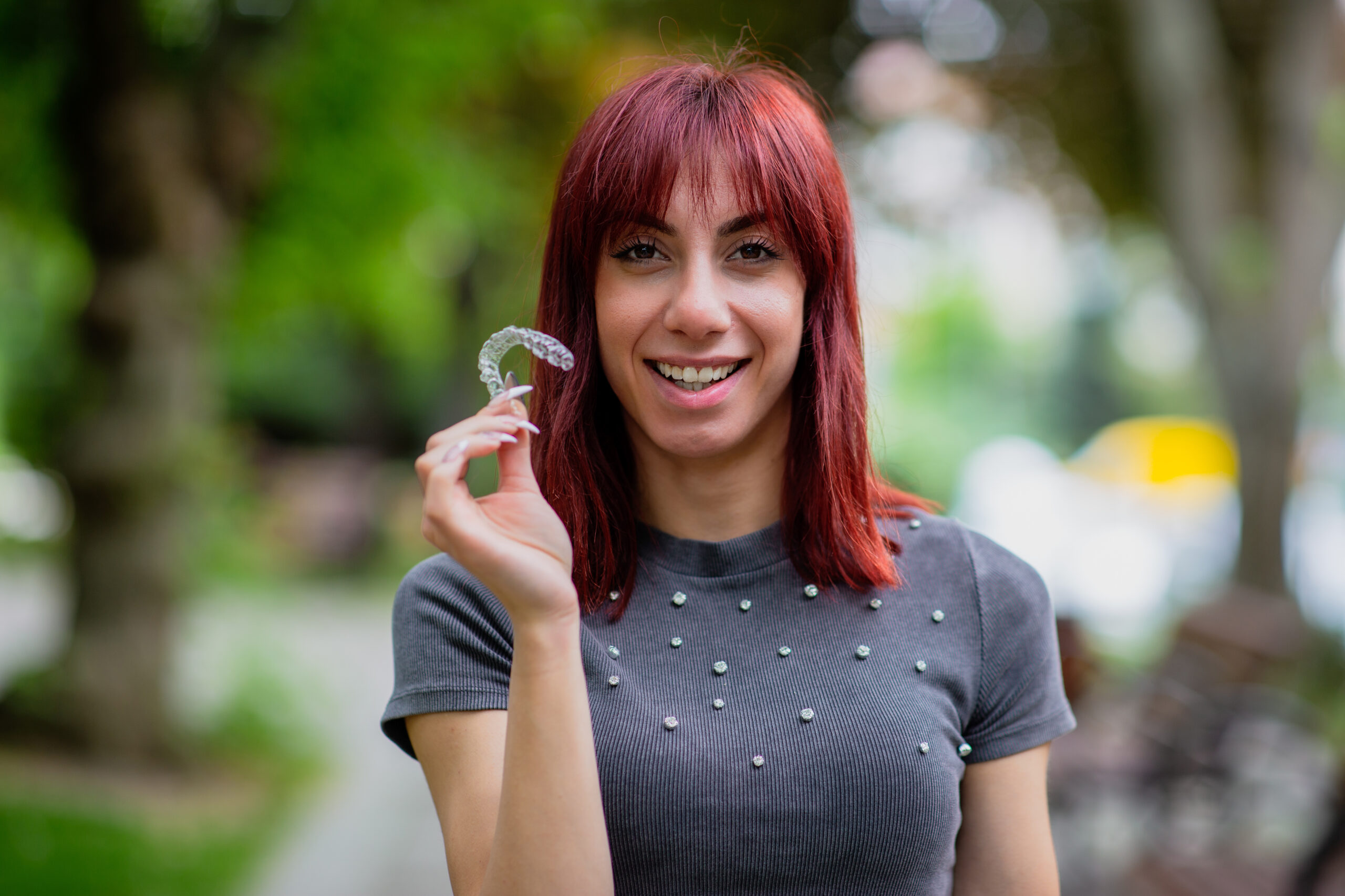 Woman smiling while holding Invisalign clear aligners before starting treatment for severe bite problems.